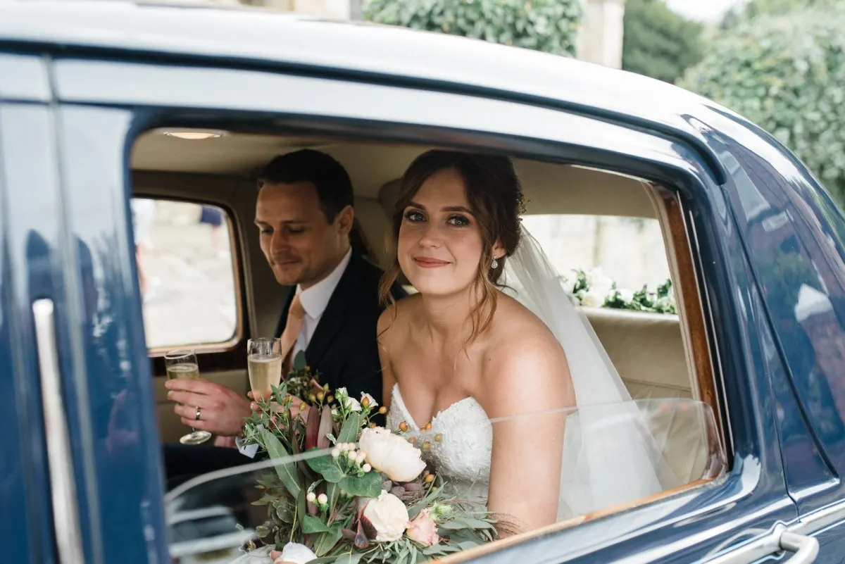 Bride and groom in a quiet embrace by a draped window, black and white
